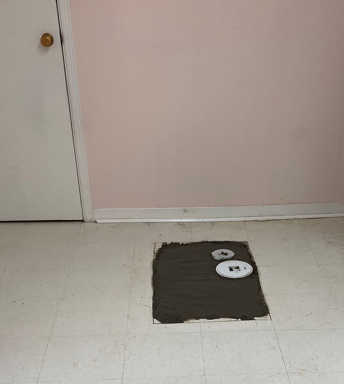 Basement floor patched with concrete over a backwater valve, access covers visible